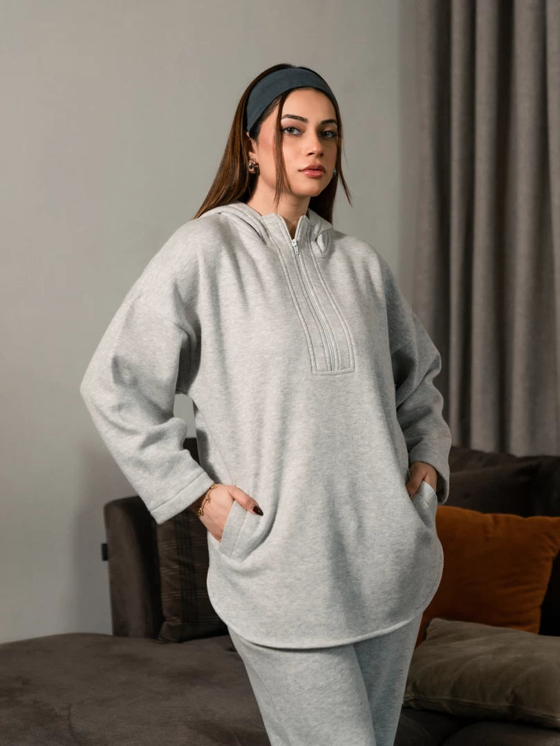Closer view of the Darya Heather Grey oversized hoodie showing the extended zipper and front pockets, with both hands in the pockets.