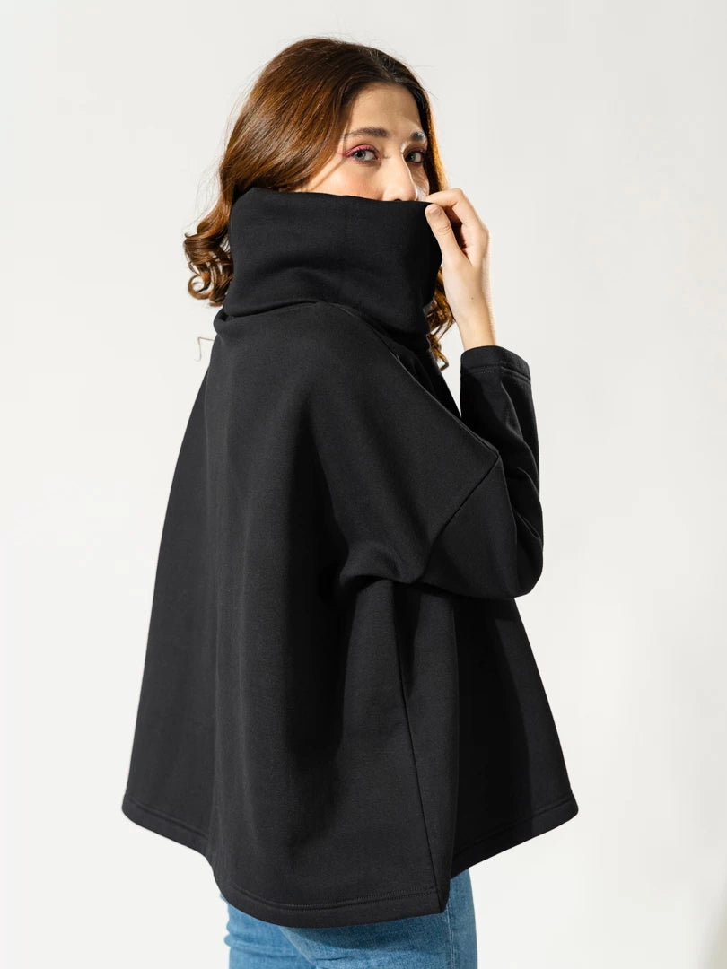 Side and back view of the Elkin black high-neck sweatshirt, showing its loose, boxy shape as the model lifts the collar near her face.