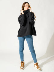 Model standing in the Elkin black winter sweatshirt and blue jeans, with one hand raised to its tall, folded neckline.