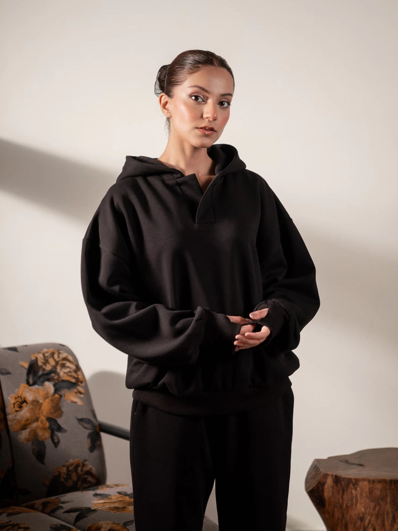 Front view of the Garconne women's black cotton fleece hoodie, modeled with hands clasped to show its oversized body and long sleeves.