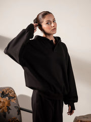Model wearing the Garconne oversized black hoodie with one hand raised beside her head, showing its loose sleeves and relaxed fit.