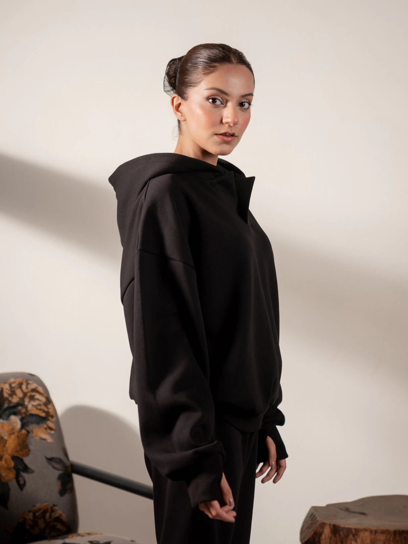 Side profile of the Garconne black winter hoodie, highlighting its raised hood shape, dropped shoulders and loose-fitting sleeves.