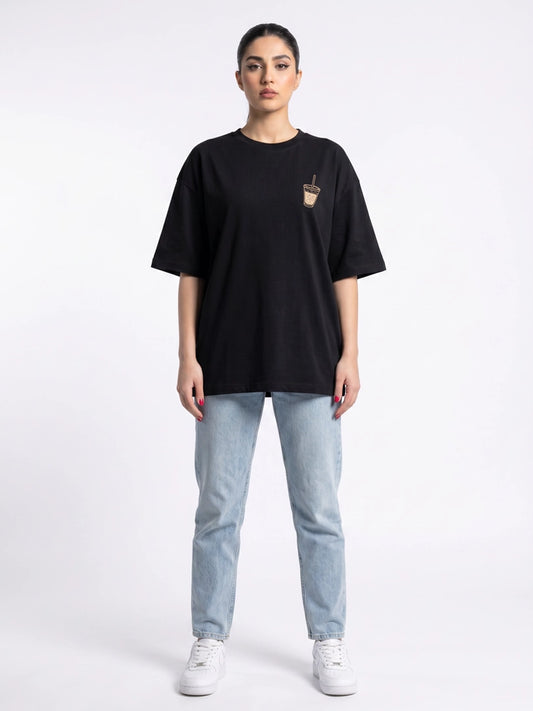 Front view of Coastline's Iced Coffee Oversized Tee in Black, showing its relaxed fit and small chest graphic, styled with light blue jeans.