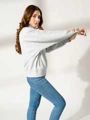Side view of the Kai American Heather Grey sweatshirt, styled with blue jeans as the model extends her arms to show the relaxed fit.