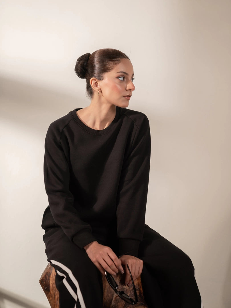 Model seated wearing the Lana Black striped sweat set with matching sweatshirt and wide-leg trousers