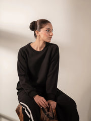 Model seated wearing the Lana Black striped sweat set with matching sweatshirt and wide-leg trousers