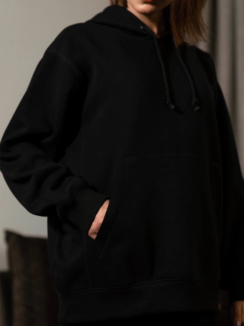 Close-up of the Lynn oversized Black hoodie showing the front pocket opening and relaxed fit around the waist.
