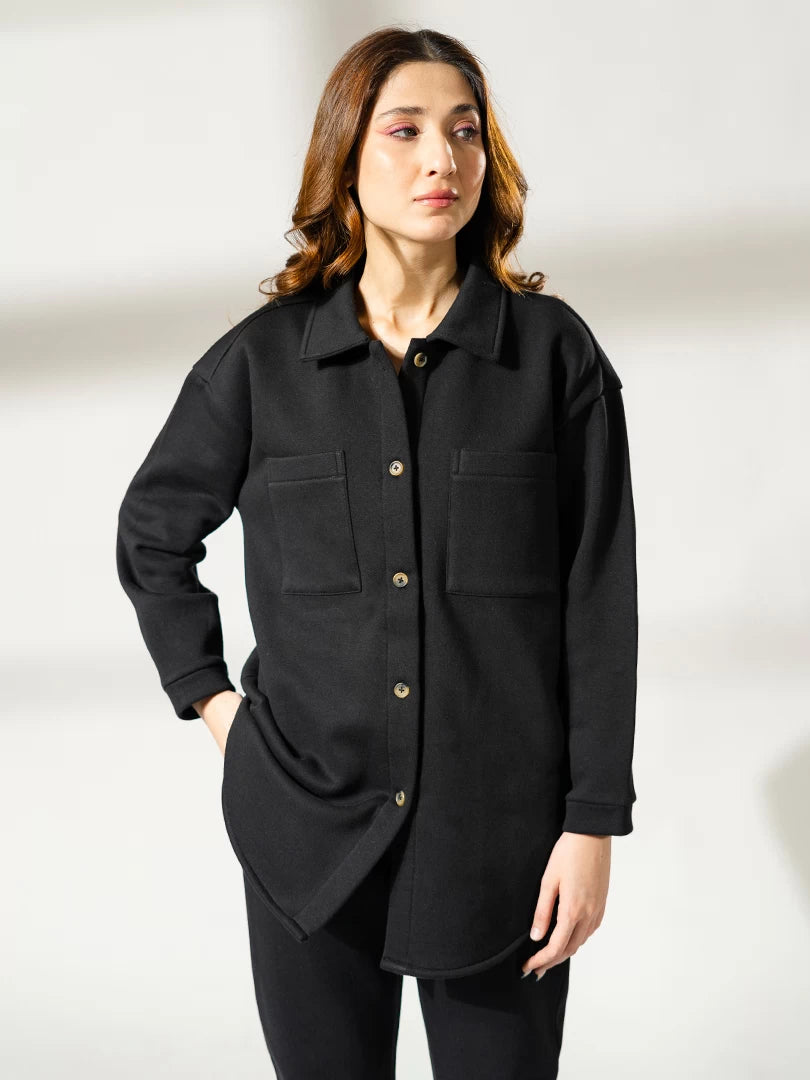 Closer front view of the Maru black shacket showing the collar, front pockets and button opening, with one hand at the hip.
