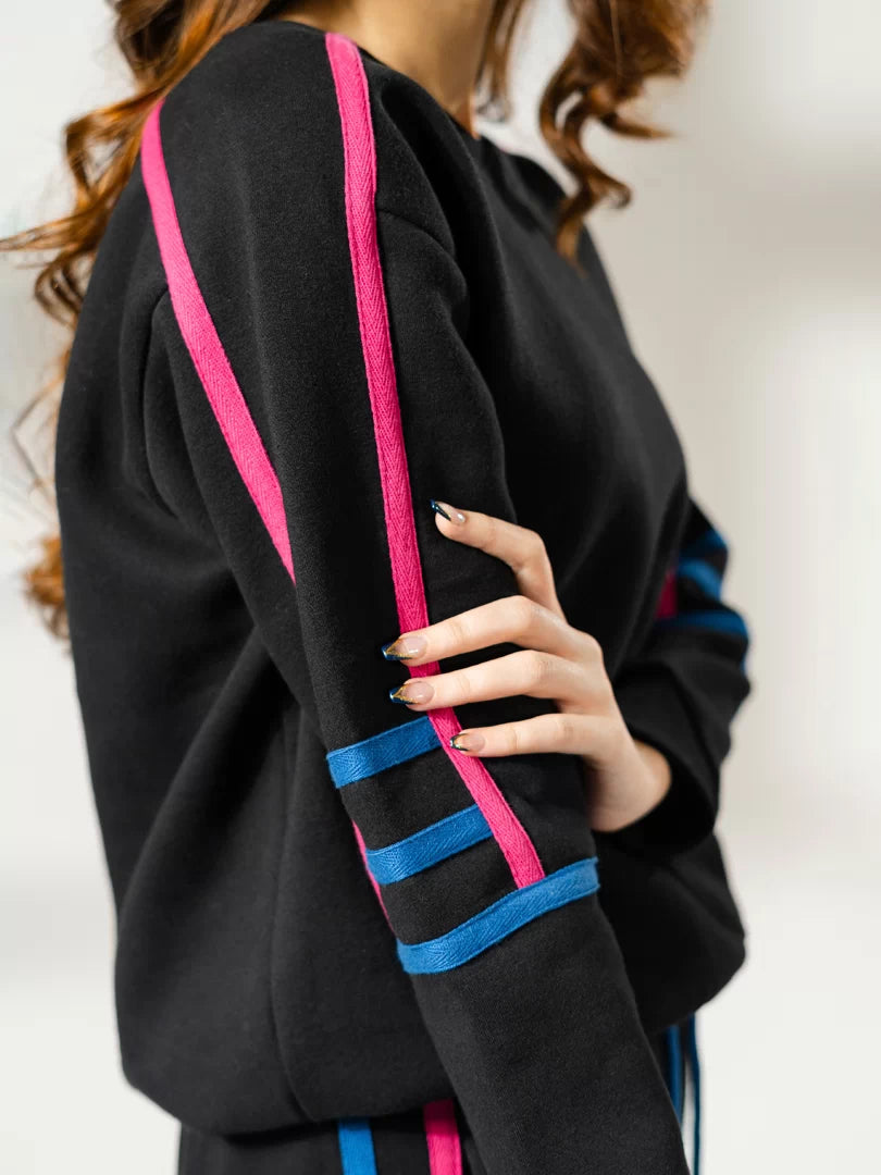 Close-up of the Michi Black fleece sweatshirt featuring pink and blue contrast tape along the sleeve.