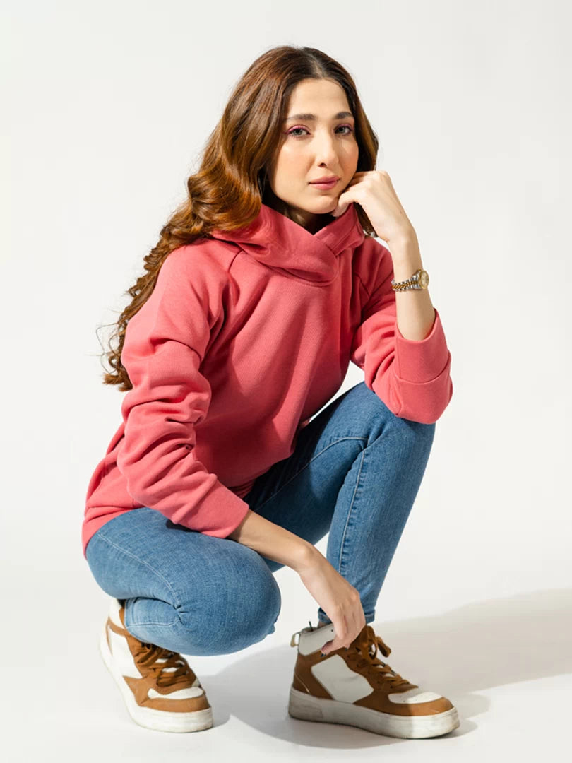 Model crouching in the Naia Lychee Pink hoodie, showing its relaxed fit, long sleeves and hood.
