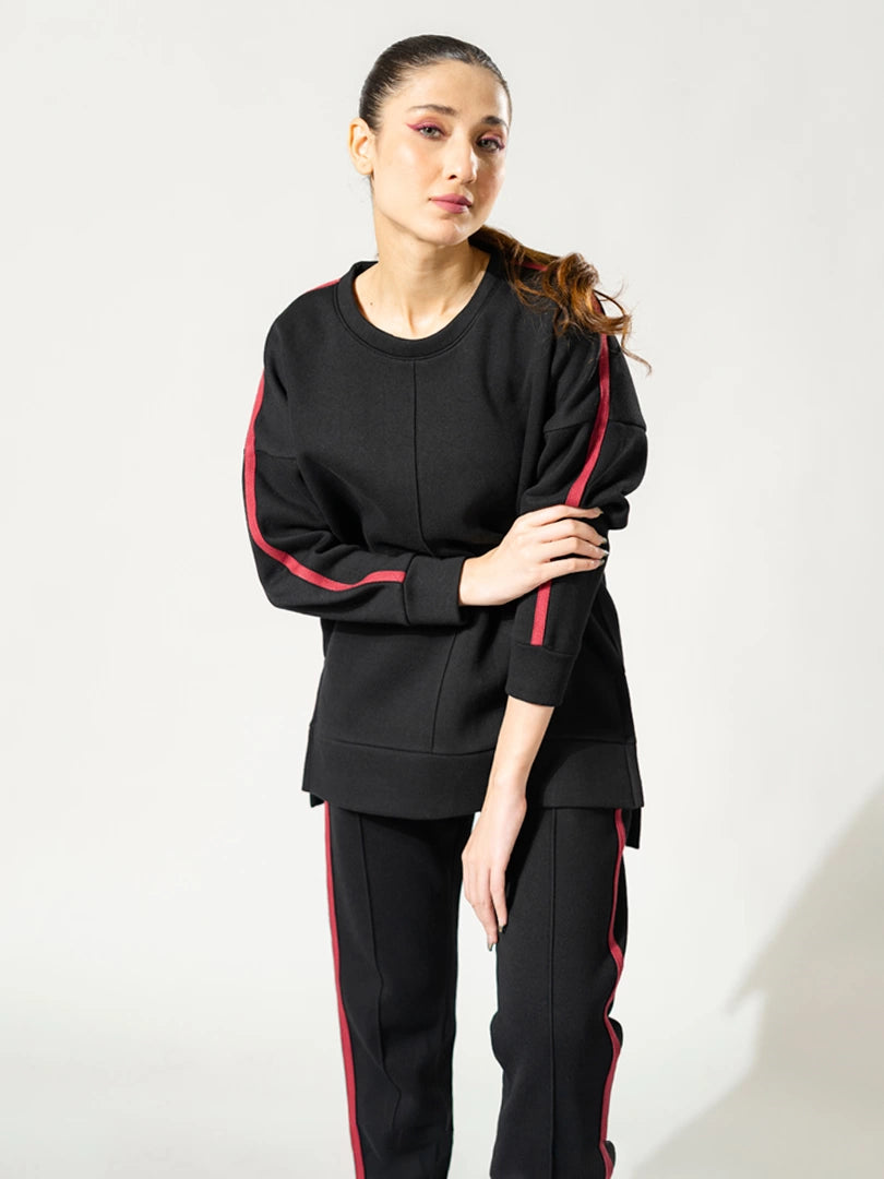 Angled view of the Ora black athleisure top showing its loose fit, round neckline and contrasting sleeve detailing.