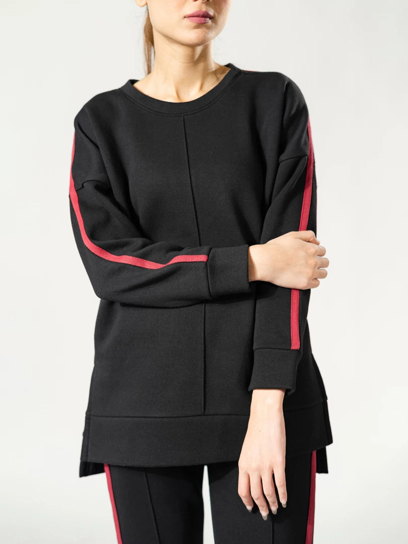 Close-up of the Ora black top showing contrasting tape along the sleeve and the loose-fitting hem.