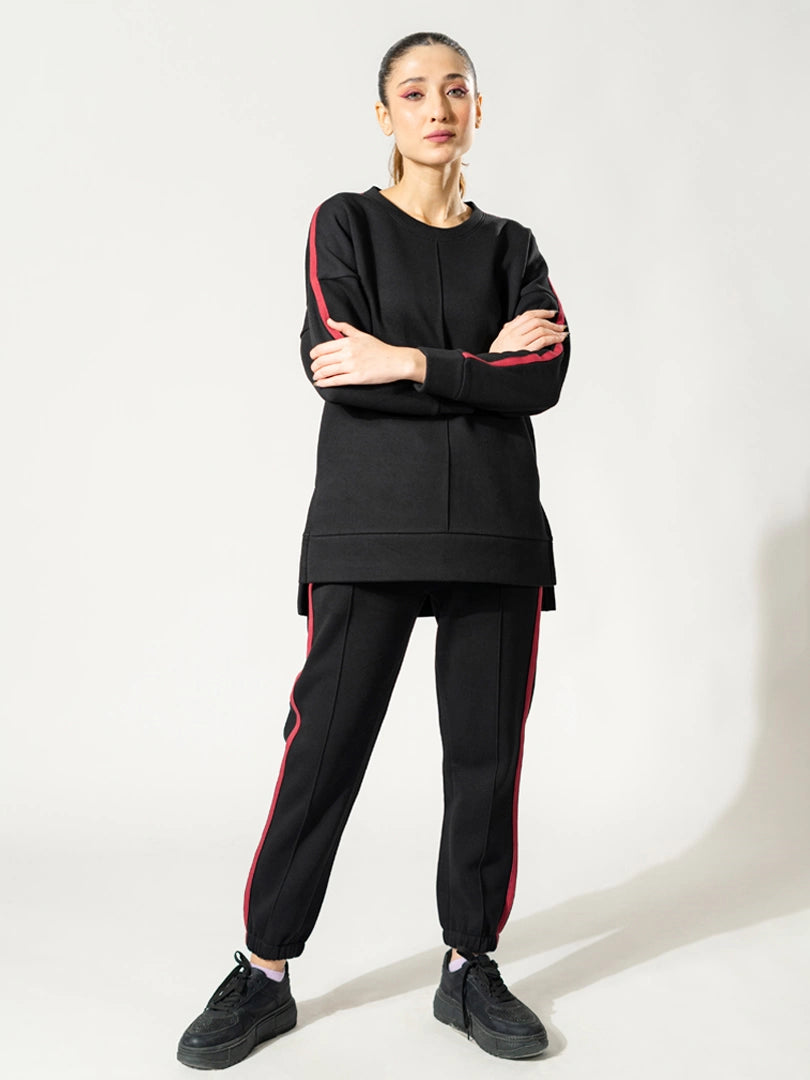 Model wearing the Ora black winter athleisure set with arms crossed, showing the loose top and contrasting sleeve and trouser detailing.