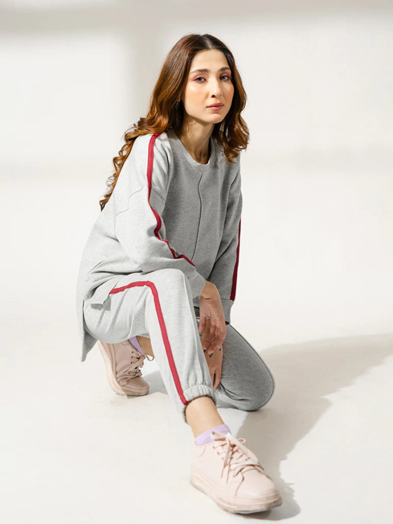 Seated model in the Ora Heather Grey matching set with purple contrast detailing on the sweatshirt and trousers