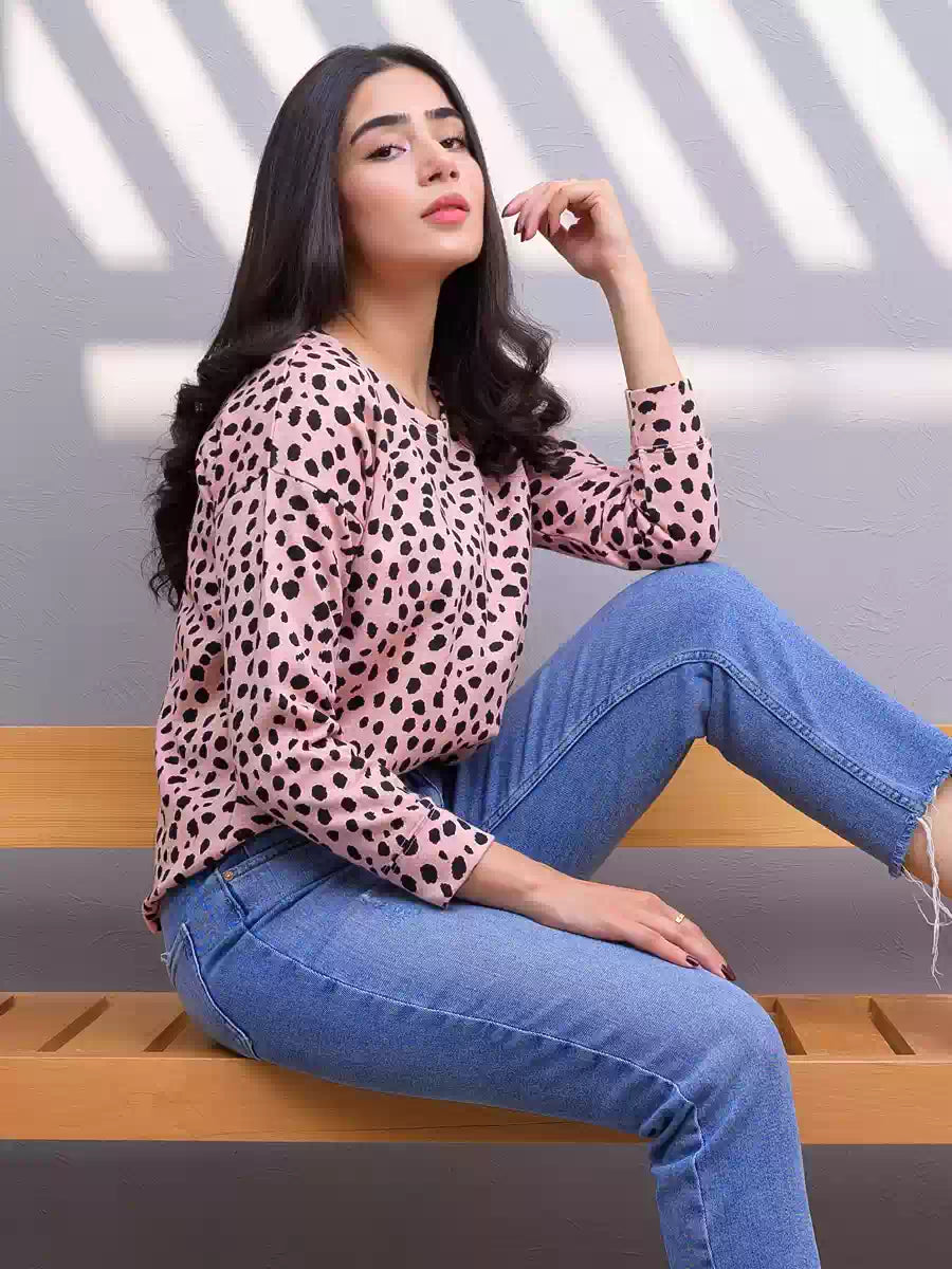 Side view of the Heather Pink animal print sweatshirt as the model sits on a wooden bench wearing blue jeans.