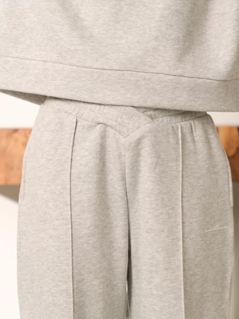 Close-up of the Soho Heather Grey trousers showing front pleats and the waistband beneath the hoodie hem.