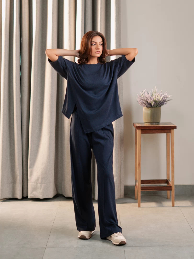 Model wearing the Sorelle Oxford Blue oversized co-ord set with a loose top and wide-leg trousers, with both hands behind her head.