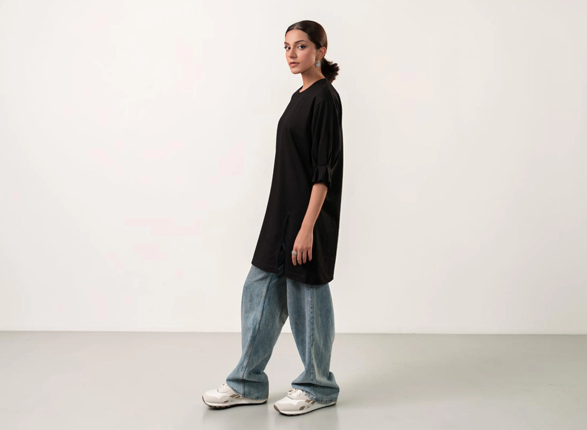 Person wearing a black oversized shirt and blue jeans standing against a white background
