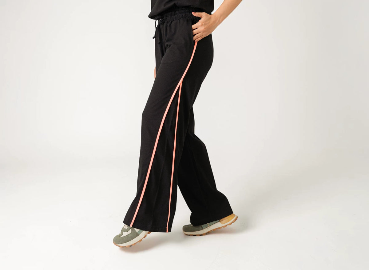 Model wearing black wide-leg women’s trousers with pink side stripes