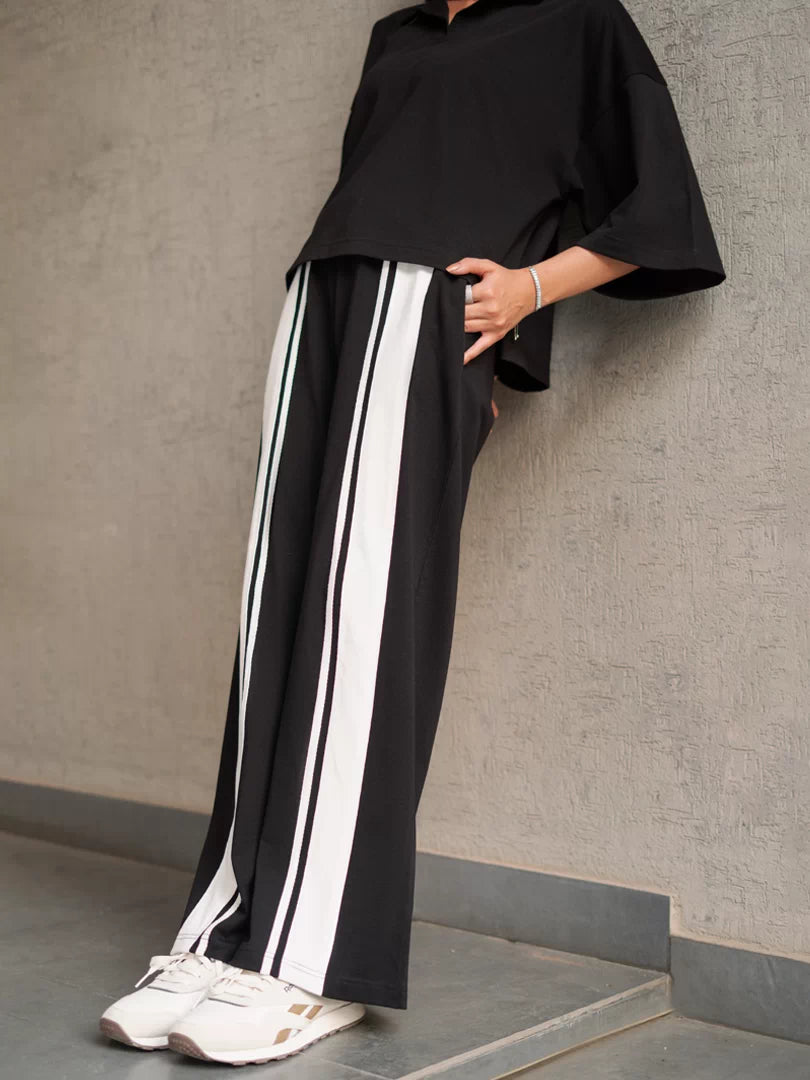 Close-up of the Zane black wide-leg trousers showing contrasting side stripes, with the model's hand in a pocket.