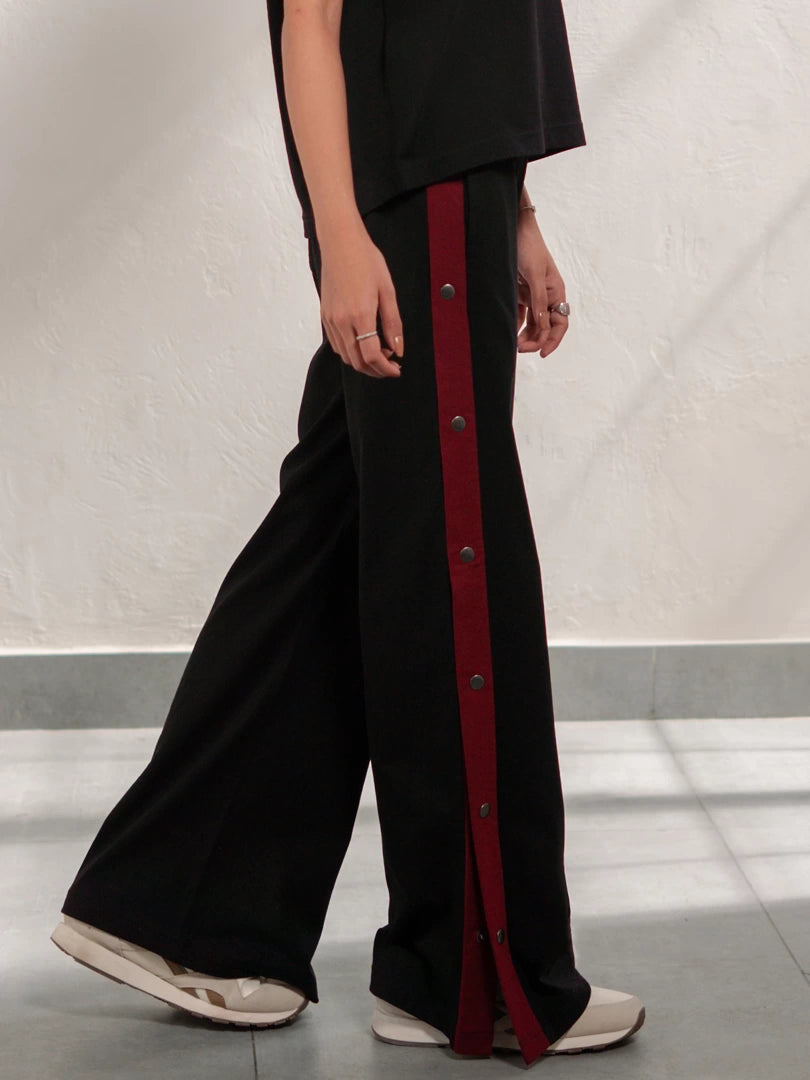 Side view of the Zoey Black wide-leg trousers showing the contrast red stripe and split-hem design.