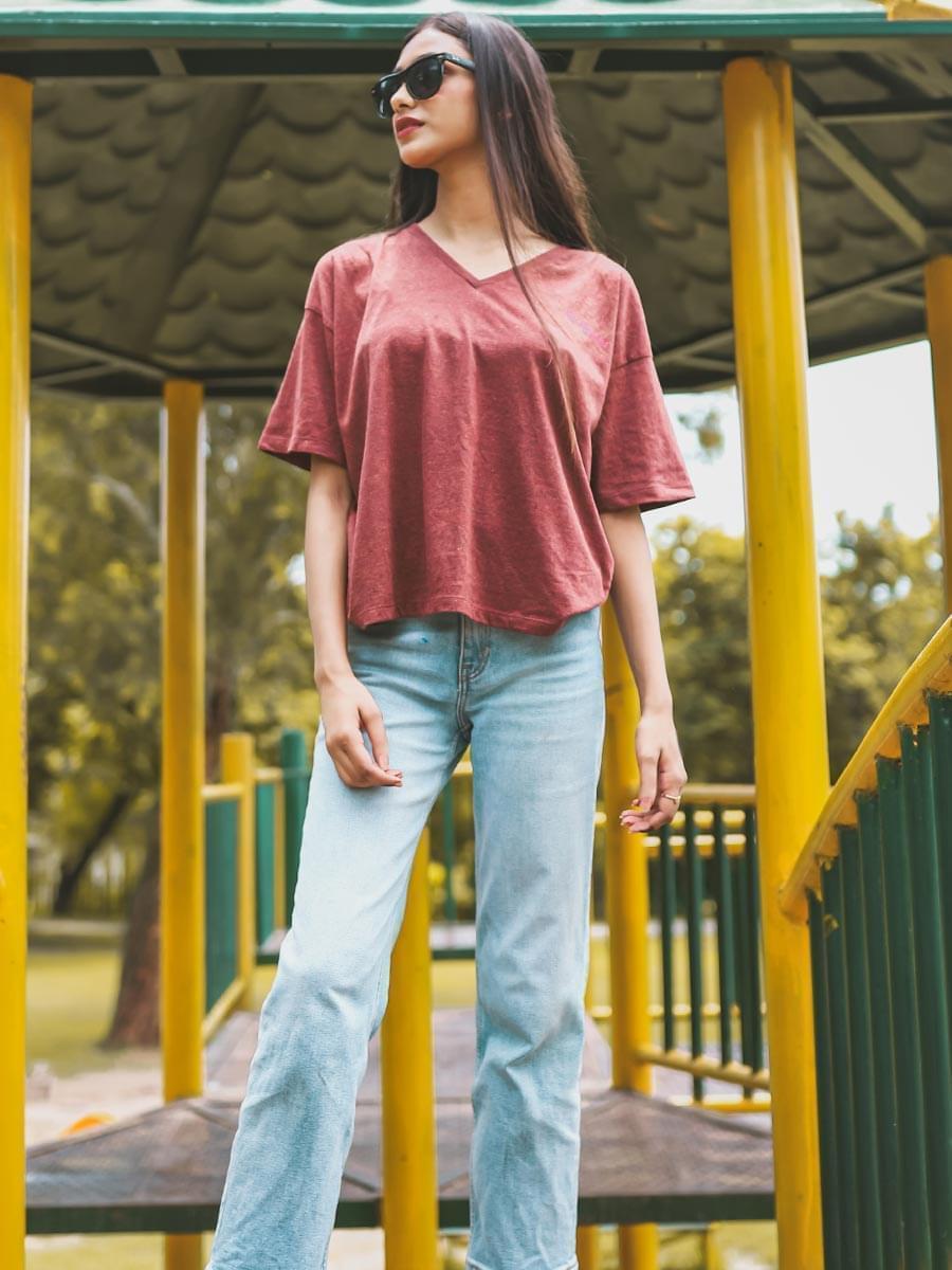 Full-length outdoor view of the Beach Club Rosewood Red oversized cotton tee, styled with light blue wide-leg jeans and sunglasses.