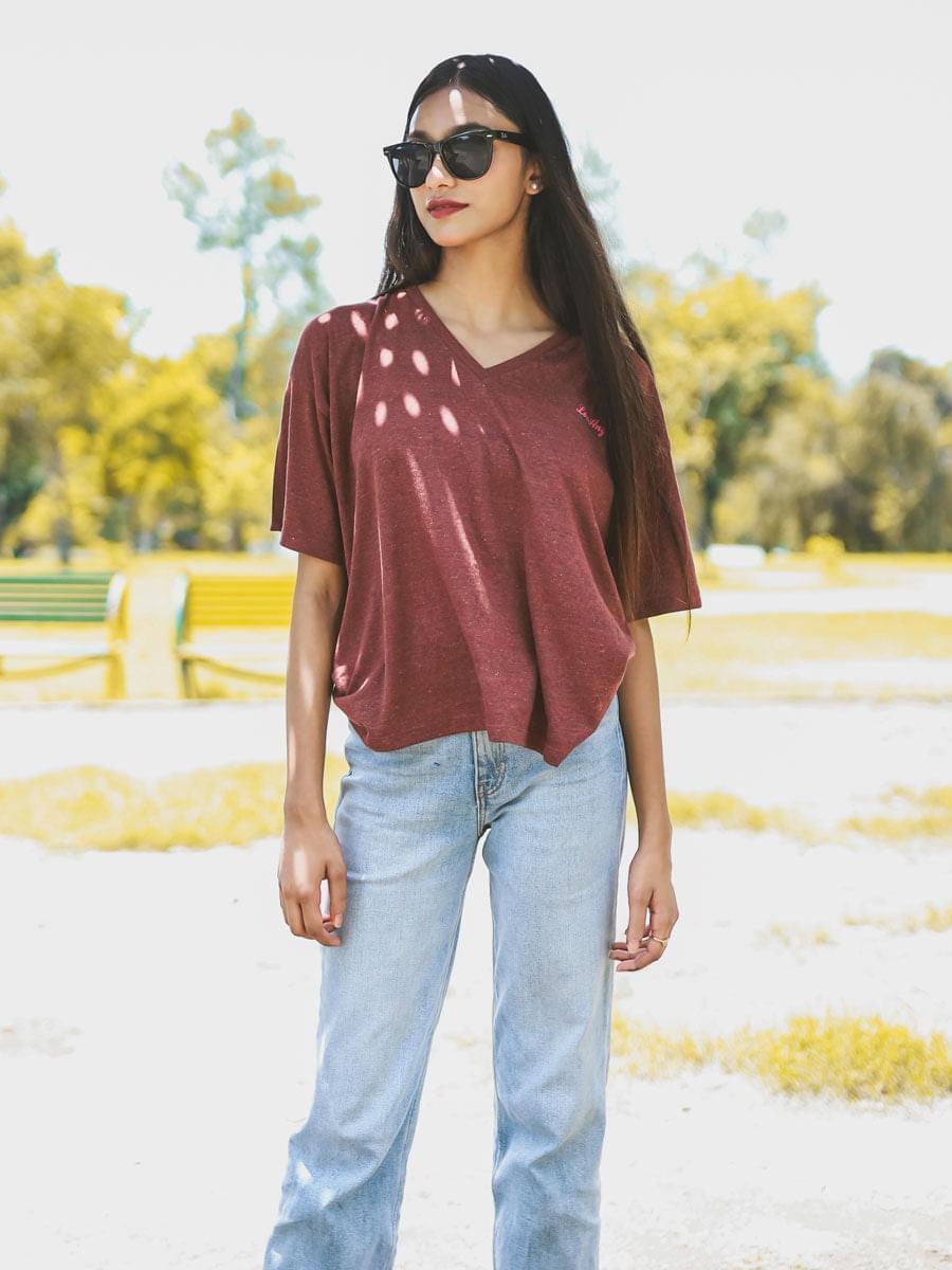 Model wearing Coastline's Beach Club Oversized Top in Rosewood Red, featuring dropped shoulders and a loose fit in an outdoor fashion shoot.