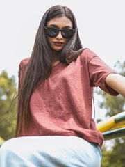 Model seated outdoors wearing Coastline's Beach Club Oversized Top in Rosewood Red, showing its wide short sleeves and relaxed drape.